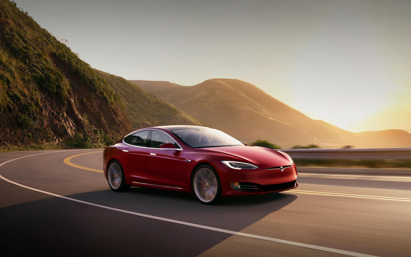 A red Model 3 Tesla electric car driving in the sunset